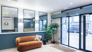 A modern lobby with a sofa, large mirrors, a potted plant, and a view of the street outside. - Hotel De Venise (Paris)