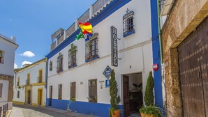 A building with a blue and white facade, a sign reading "HOSTAL," and a flag hanging above the entrance. - Arc House Cordoba (Córdoba)