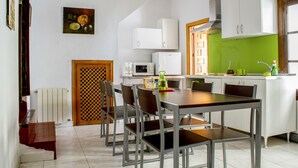 A modern kitchen with white cabinets, a dining table with chairs, a microwave, and a green backsplash. - Arc House Cordoba (Córdoba)