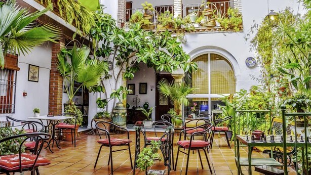 An indoor courtyard with multiple tables and chairs, surrounded by lush greenery and potted plants. - Arc House Cordoba (Córdoba)