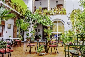 Un patio interior con varias mesas y sillas, rodeado de abundante vegetación y plantas en macetas.