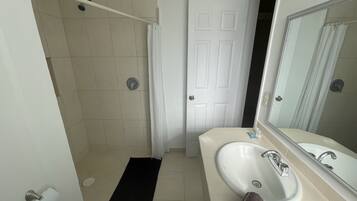 Een badkamer met douche, toilet, wastafel en spiegel.