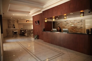 Zona de recepción de un hotel con un mostrador de madera, un espejo grande y una pared de piedra.