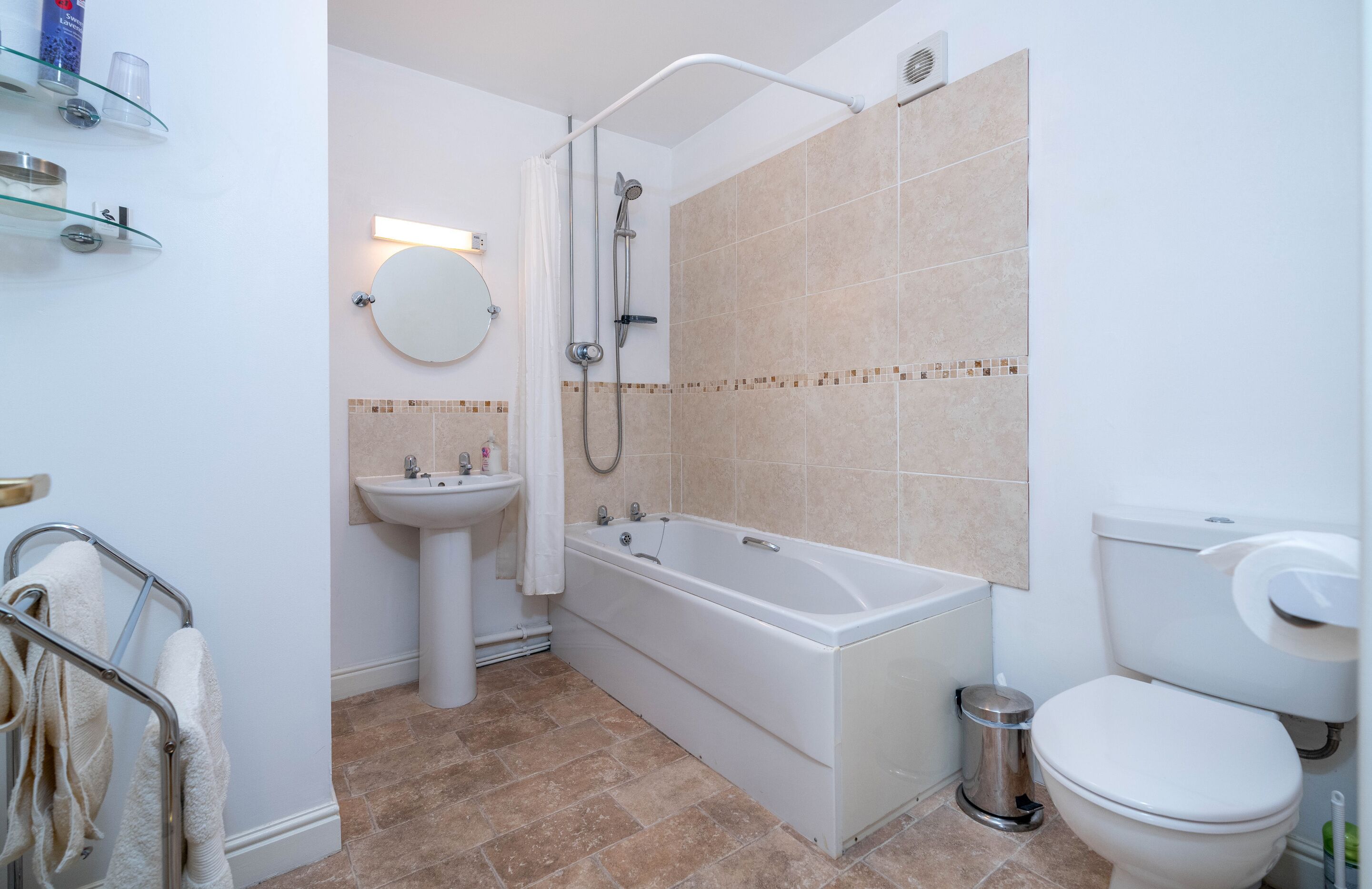 A modern bathroom with a bathtub, sink, toilet, and glass shelves.