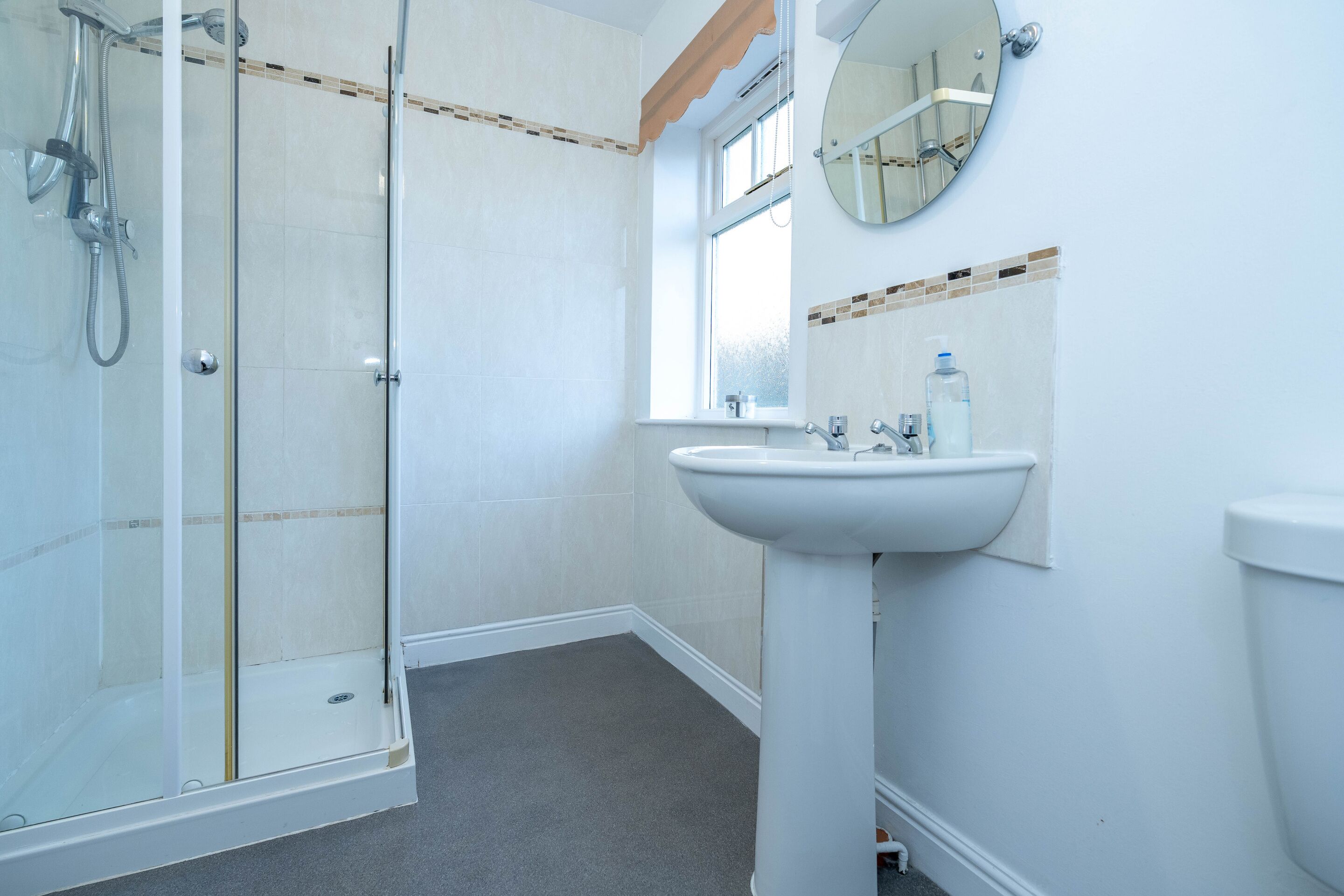 A bathroom with a glass-enclosed shower, a pedestal sink, and a window.