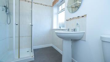 A bathroom with a glass-enclosed shower, a pedestal sink, and a window.