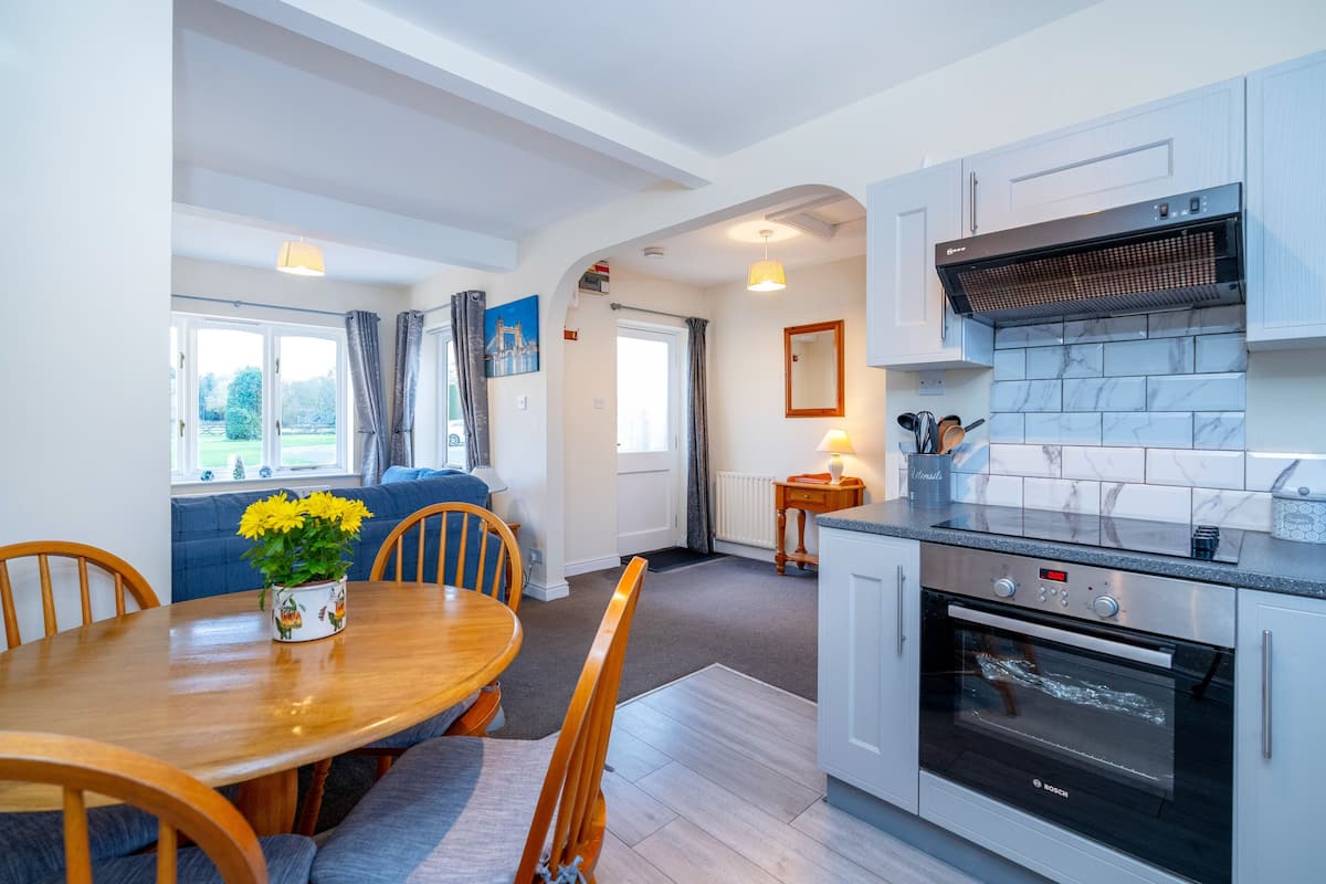 A modern kitchen with a Bosch oven, a dining area with a wooden table and chairs, and a view of the outdoors through a window.