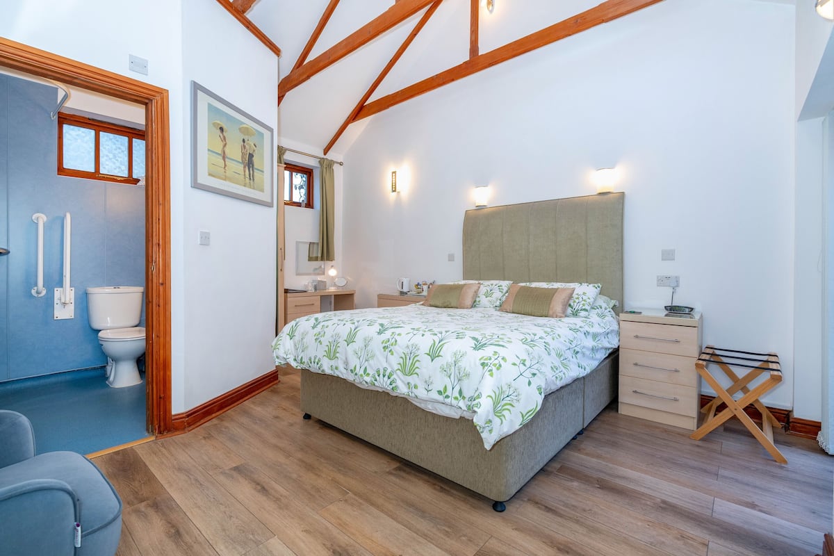 A bedroom with a bed, bedside tables, a wooden floor, a window, and a door.