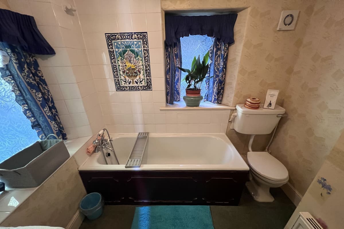 A bathroom with a bathtub, toilet, and window with curtains.