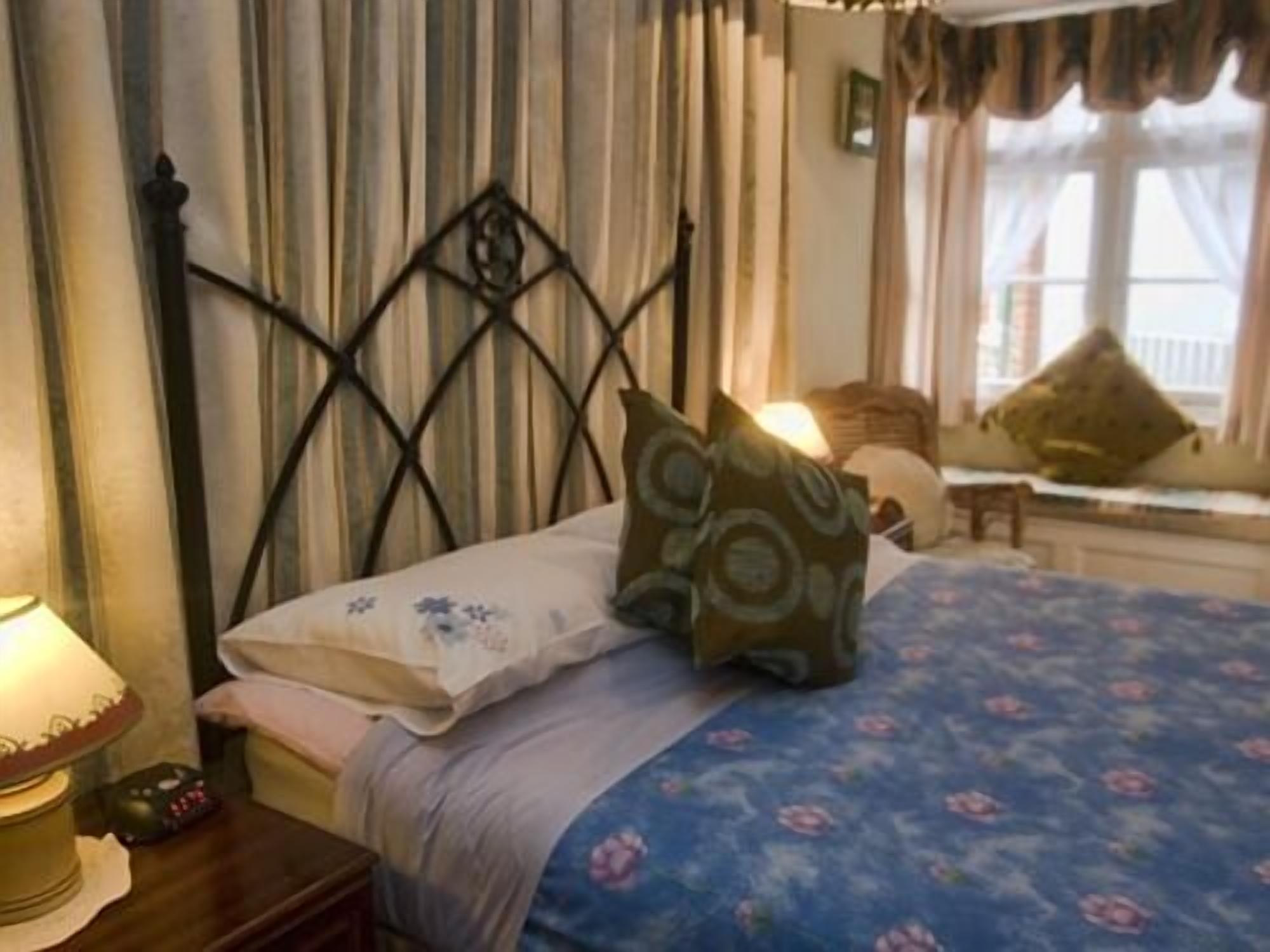 Une chambre à coucher avec un lit, des oreillers, une table de chevet, une lampe et une fenêtre avec des rideaux.