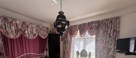 A bedroom with a bed, a vanity with a mirror, a television, and a window with curtains.