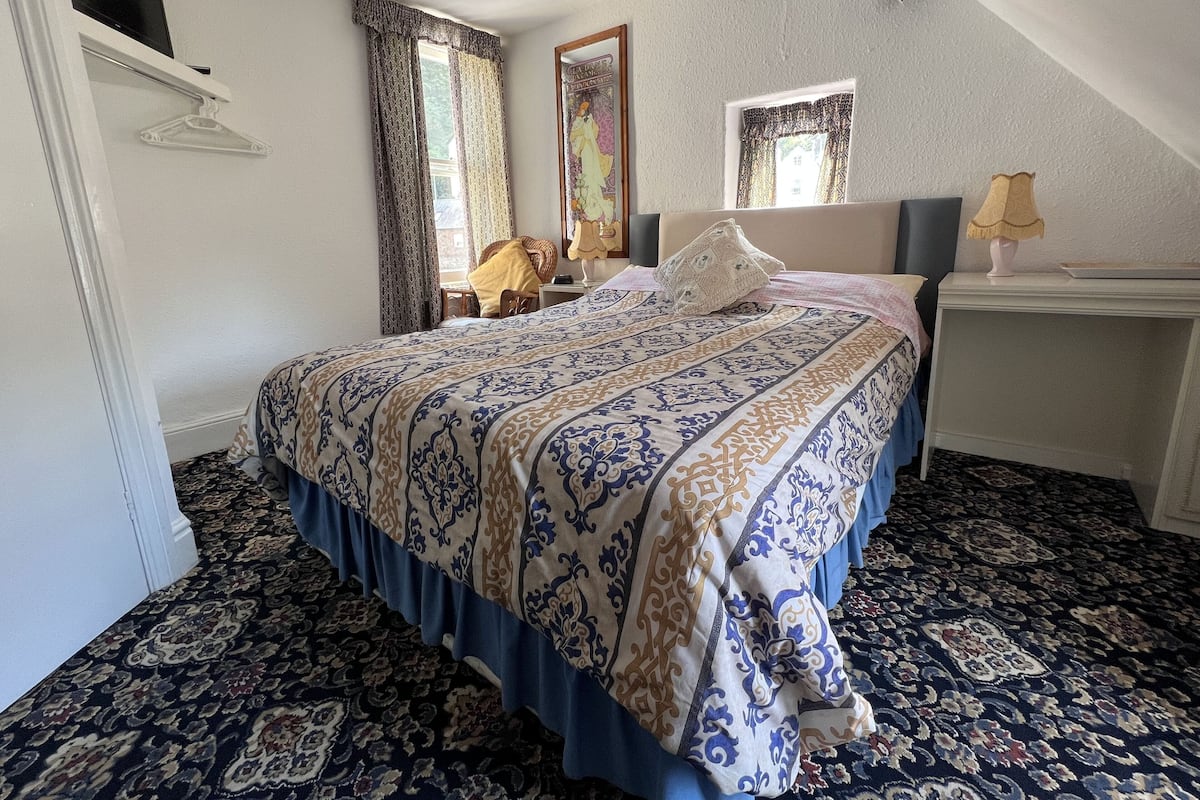 A bedroom with a large bed, a nightstand, a chair, and a window with curtains.