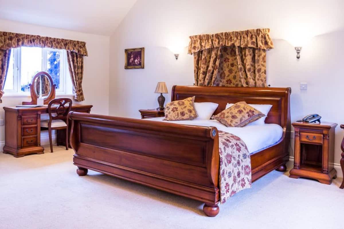 A bedroom with a wooden bed, a desk, a chair, a dresser, and a mirror.