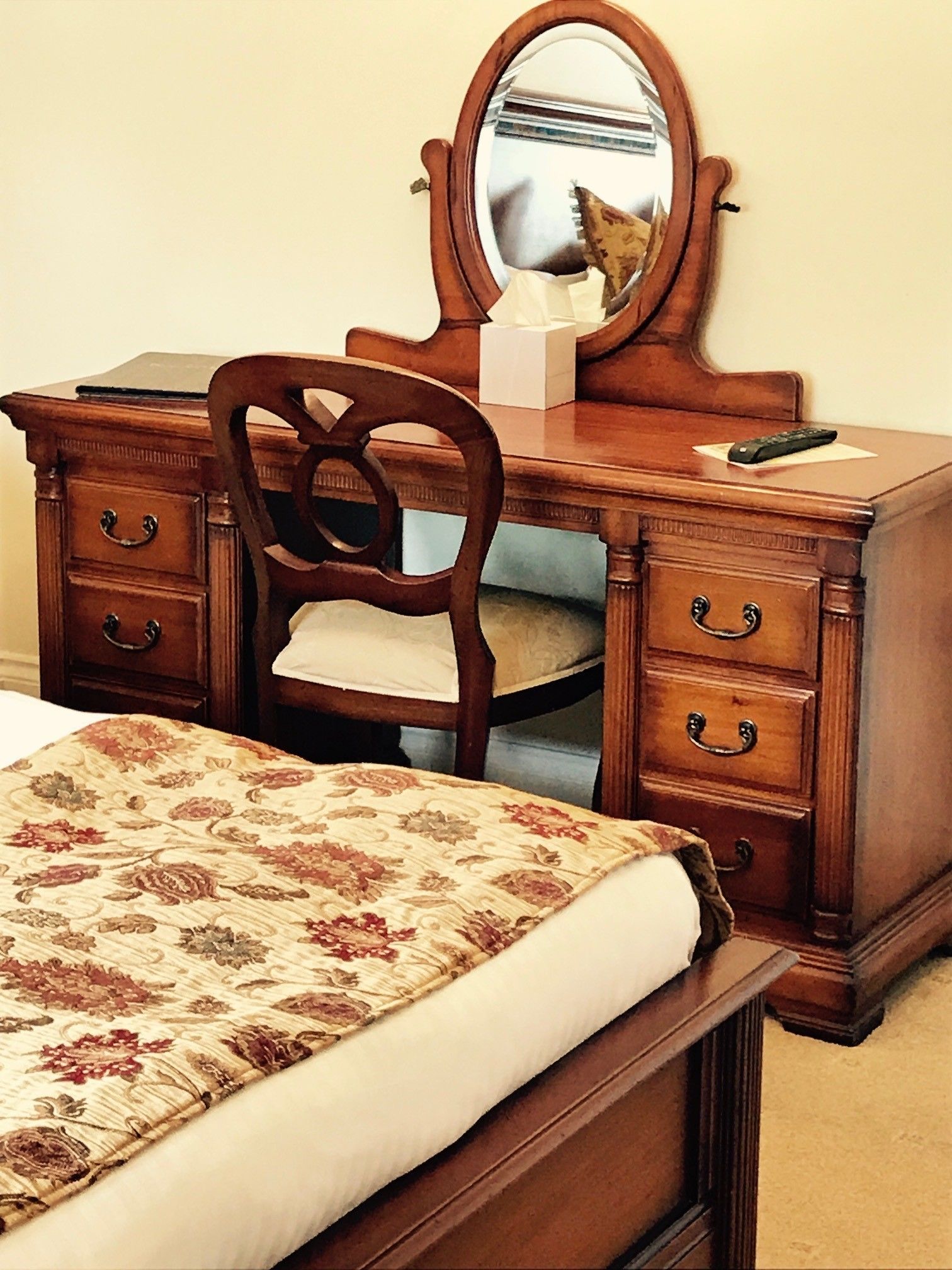 A wooden dresser with a mirror, a chair, and a bed with a floral bedspread.