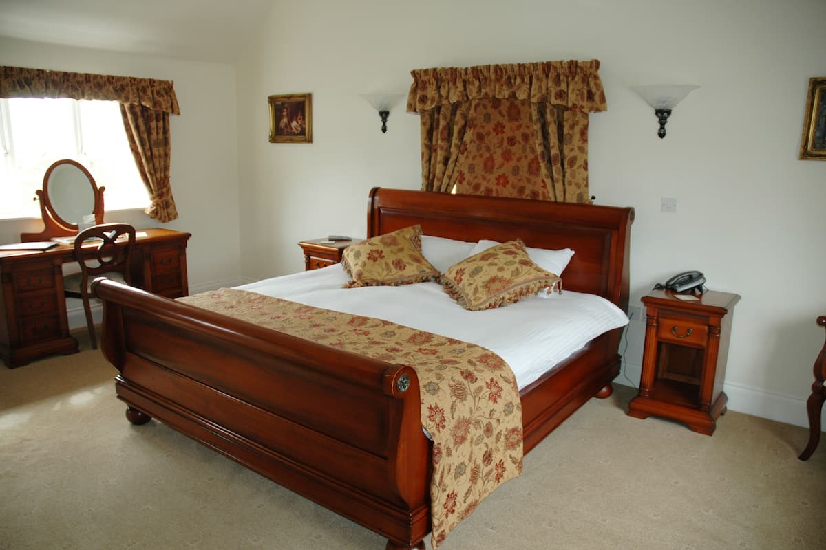 A bedroom with a wooden bed, a nightstand with a lamp, a dresser, and a mirror.