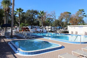 A swimming pool with lounge chairs and a sign indicating pool rules. - Orange City RV Resort (Orange City)