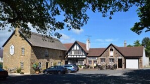 Un bâtiment traditionnel en pierre avec un toit de chaume, une structure de style Tudor avec une charpente en bois peinte en blanc et en noir, et un garage blanc.