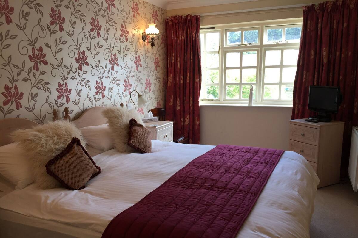 A neatly made bed with a red blanket, a fluffy pillow, and a decorative wall with floral wallpaper.