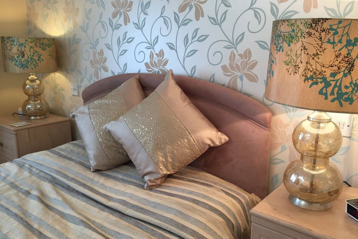 A neatly made bed with striped bedding, two decorative pillows, and a bedside lamp on a nightstand.