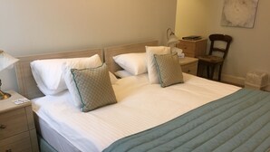 Un lit bien fait, avec du linge de lit blanc et deux oreillers, une table de chevet avec une lampe et une chaise dans une chambre d’hôtel.