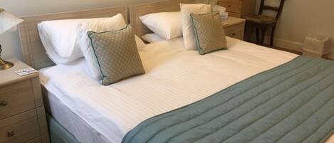 A neatly made bed with white linens and two pillows, a bedside table with a lamp, and a chair in a hotel room.