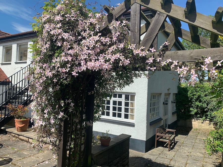 A white building with a wooden staircase and a wooden trellis covered in pink flowers.