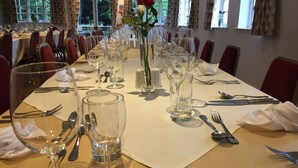 Une longue table à manger, dressée avec de nombreux verres à vin, des fourchettes, des couteaux et des cuillères, et un vase rempli de fleurs placé au centre.
