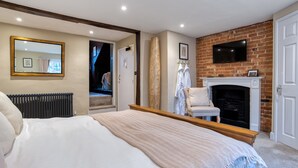 A bedroom with a large bed, a fireplace, a TV mounted on the brick wall, and a mirror on the wall. - The Grove Cromer (Cromer)