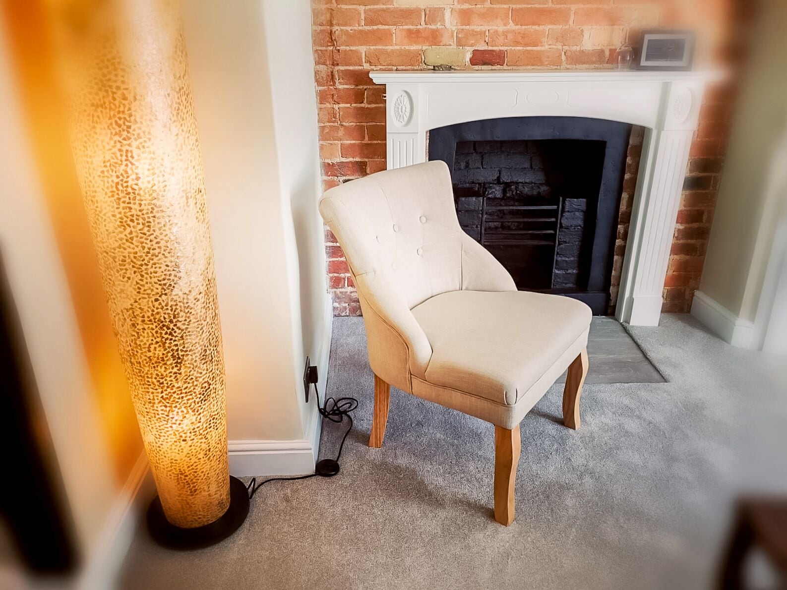 A room with a brick fireplace, a beige armchair, and a textured floor lamp.