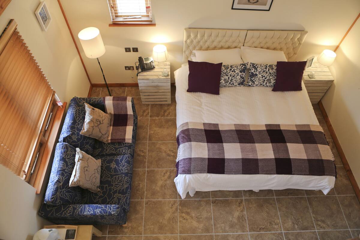 A bedroom with a large bed, a sofa, two bedside tables, and a lamp.