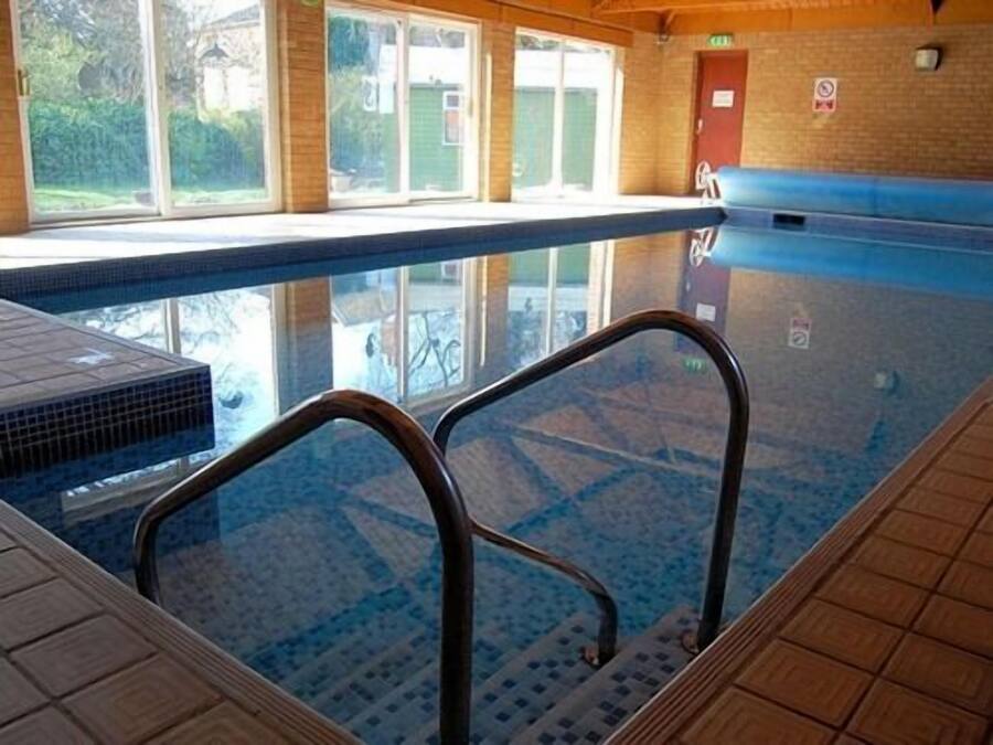 An indoor swimming pool with clear glass walls, wooden steps, and a tiled floor.
