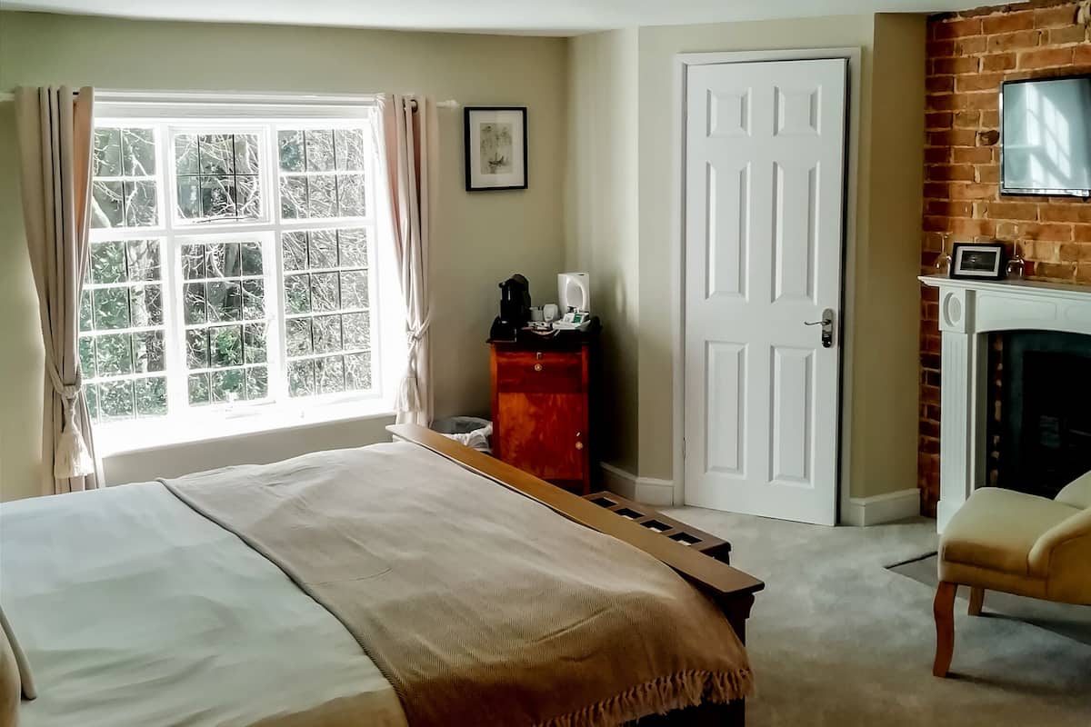 A bedroom with a large bed, a fireplace, a door, and a window with curtains.