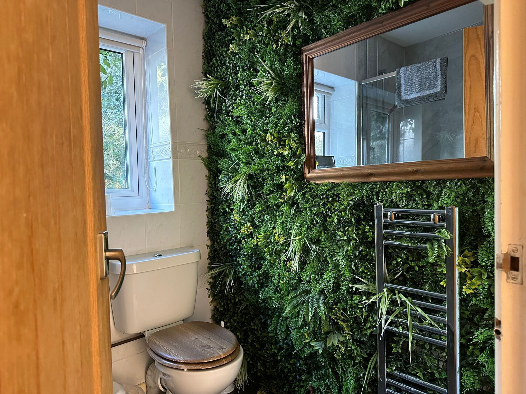 Une salle de bain avec des toilettes, un miroir et un mur recouvert de plantes vertes.