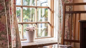 A window with a floral curtain, a potted plant, and a wooden chair with a magazine on it. - The Grove Cromer (Cromer)