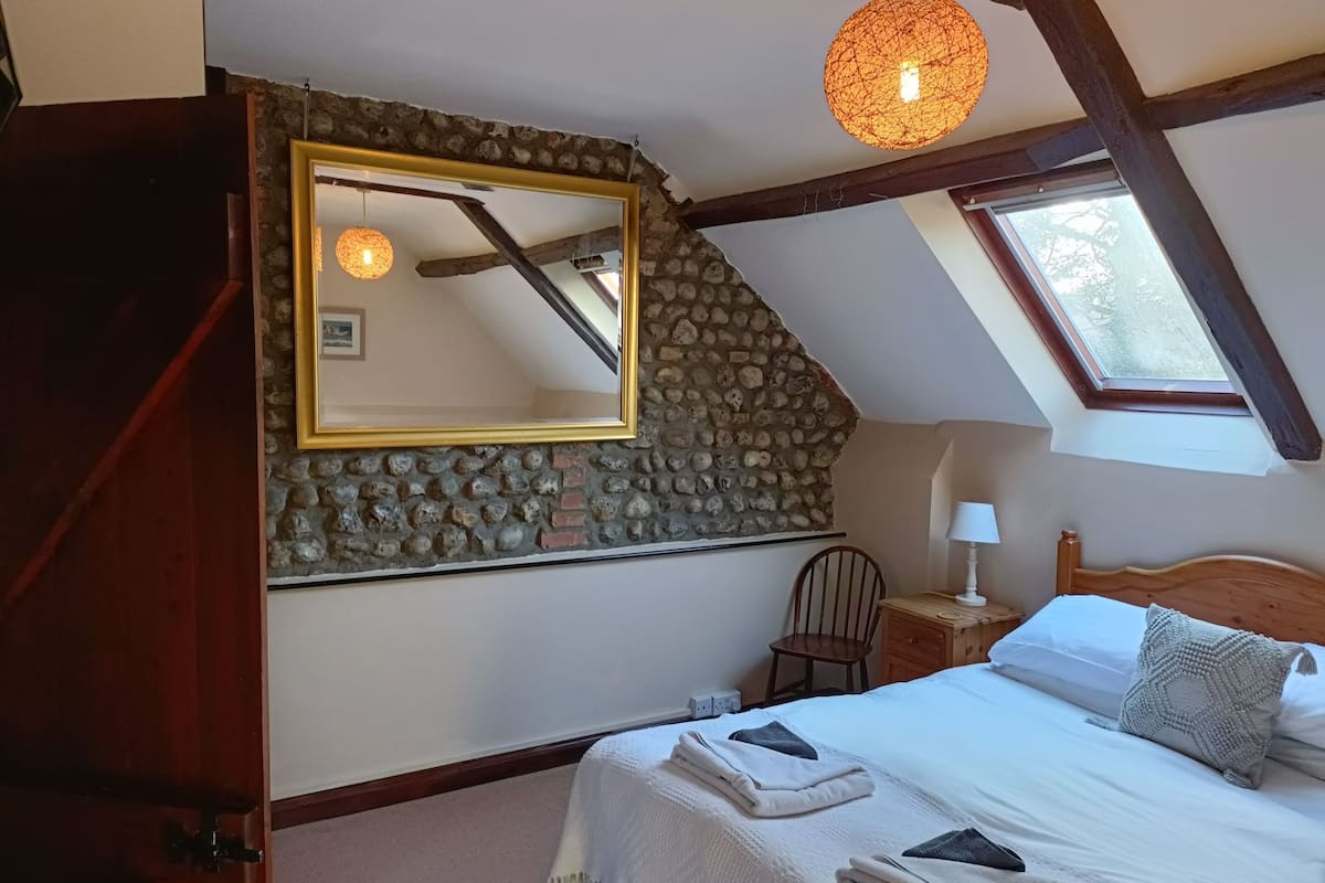 A bedroom with a stone wall, a large mirror, a wooden bed, a nightstand, and a skylight.