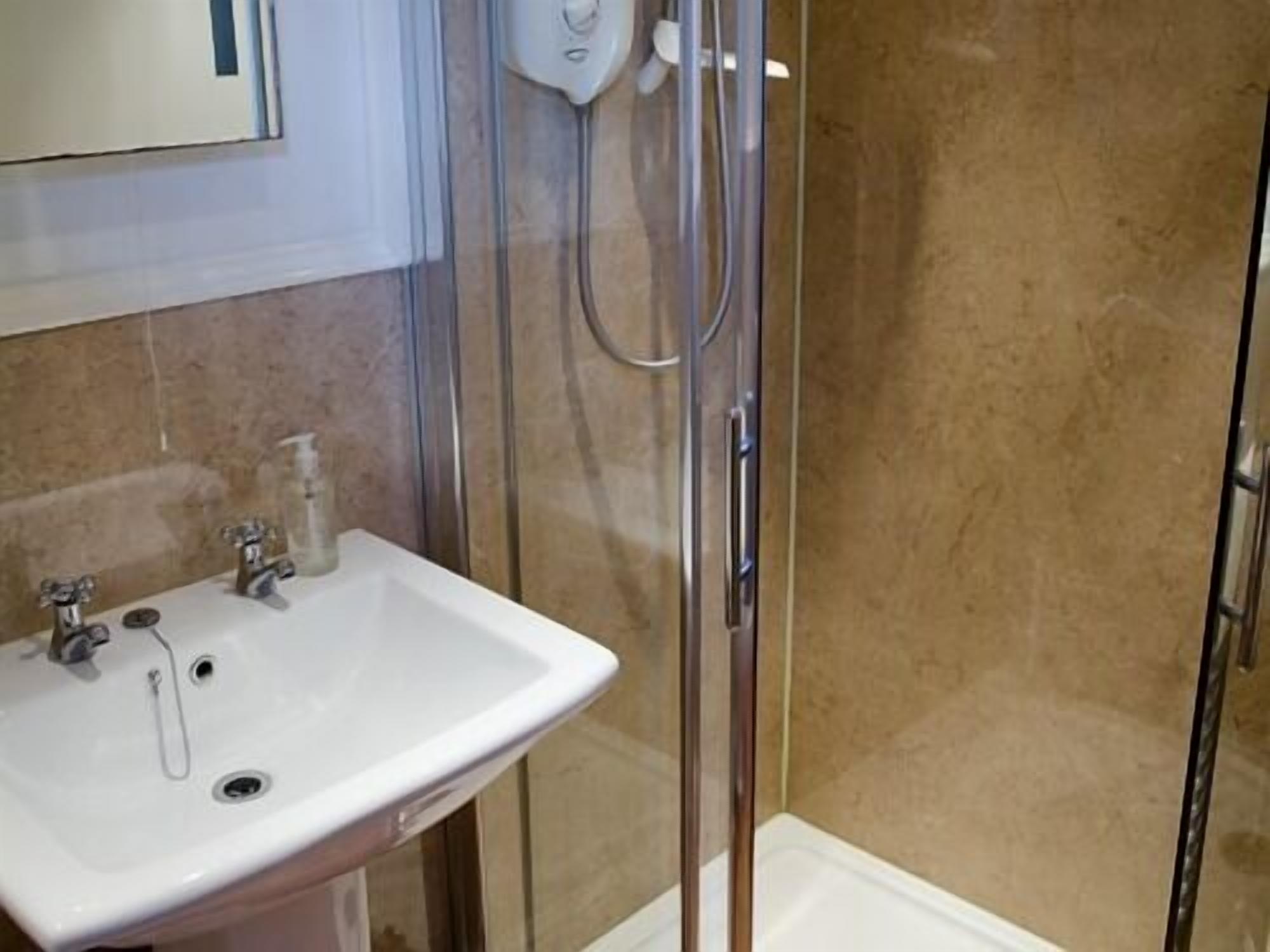 A bathroom with a glass-enclosed shower, a white sink with a soap dispenser, and a mirror above the sink.