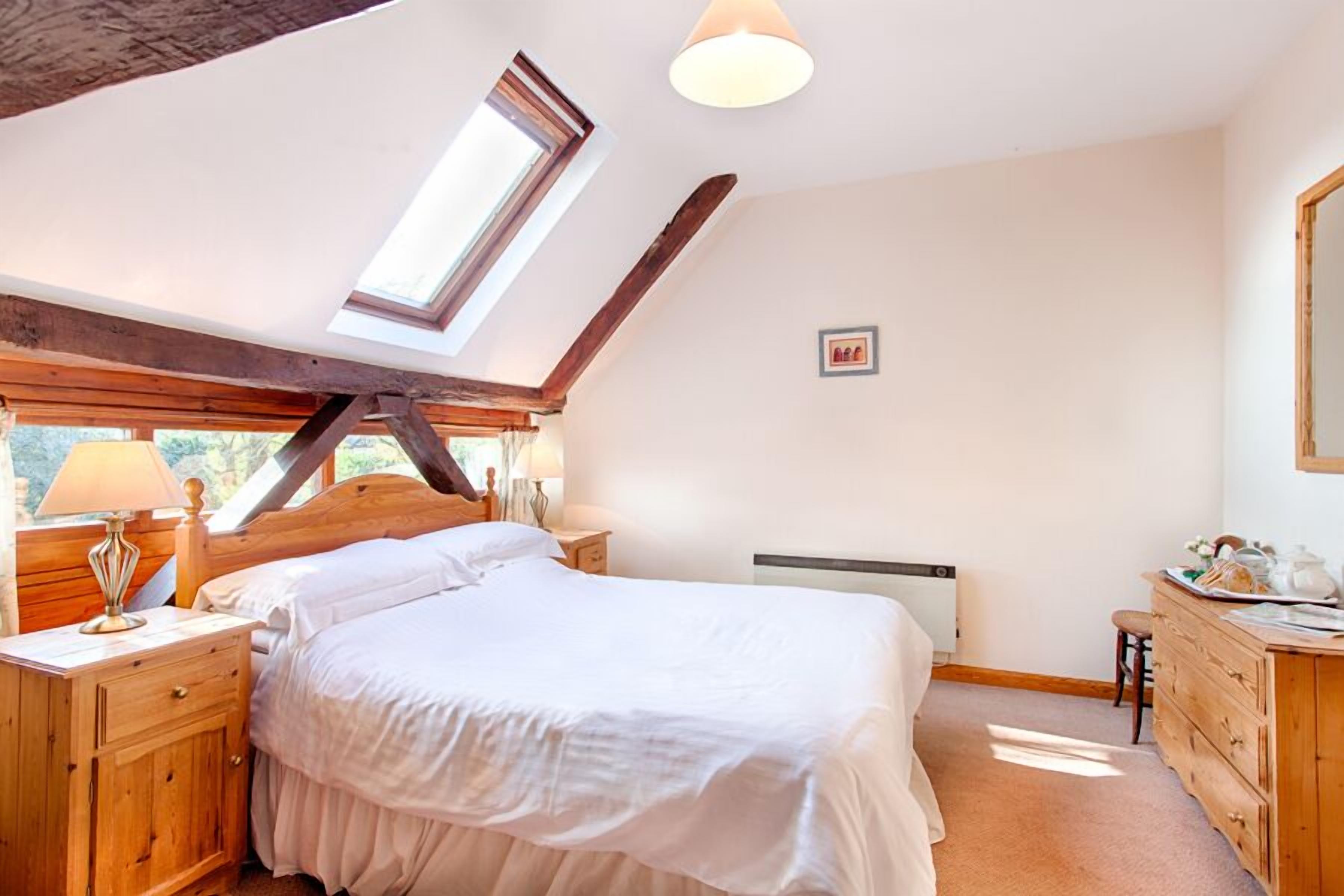 A bedroom with a sloped ceiling, a skylight, a bed, wooden furniture, and a radiator.