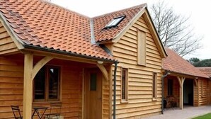 A wooden cabin with a tiled roof, a covered porch, and a small garden area with a wheelbarrow of flowers. - The Grove Cromer (Cromer)
