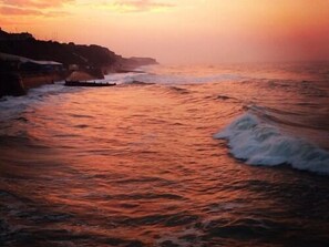 A coastal scene with waves crashing onto a rocky shore during sunset. - The Grove Cromer (Cromer)