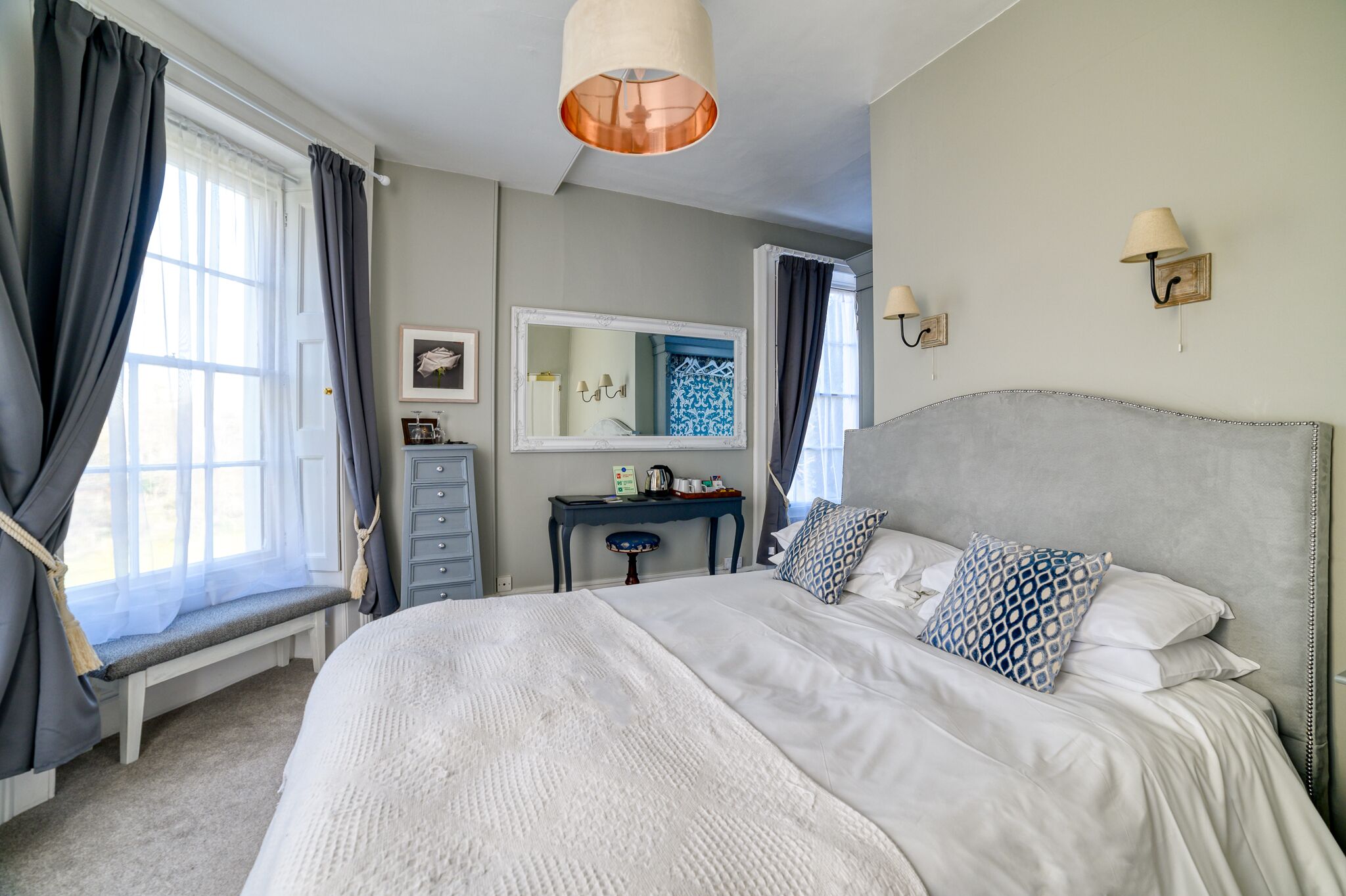 A bedroom with a large bed, a bedside table, a mirror, and a window with curtains.