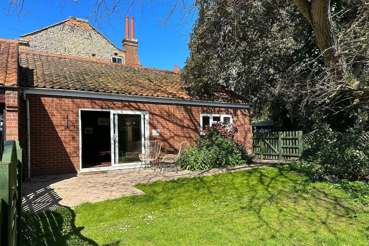 A brick house with a tiled roof, a glass door entrance, and a small garden area with a wooden fence.