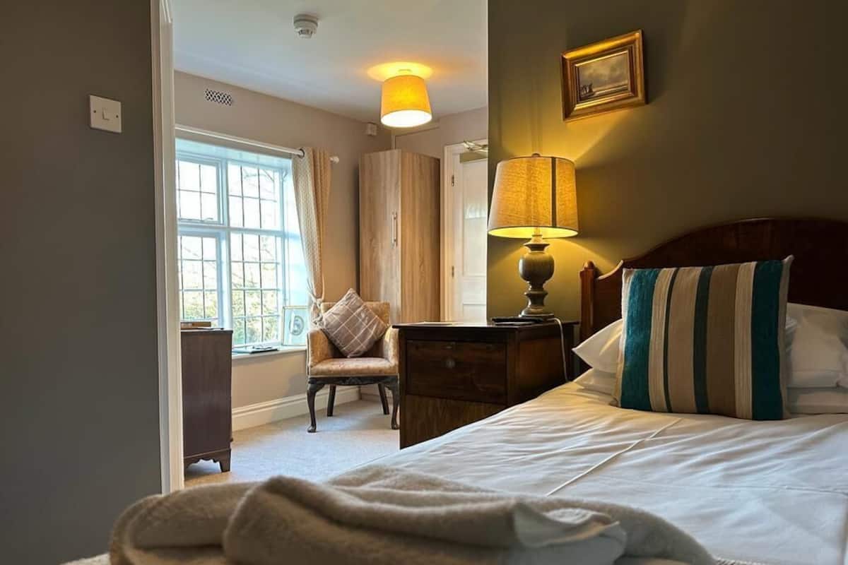 A hotel room with a bed, a nightstand, a lamp, a chair, and a window.