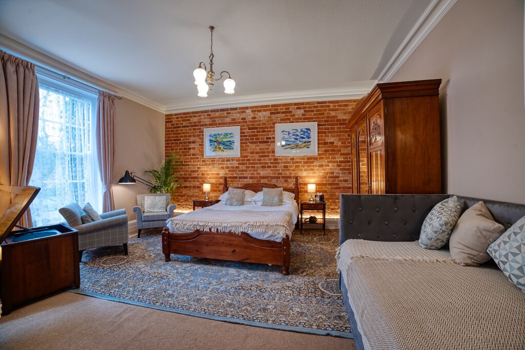 Un dormitorio con pared de ladrillo, cama, sofá, piano y un ventanal grande.