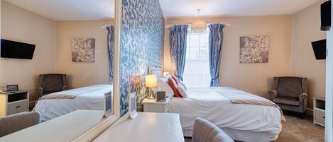 A hotel room with two beds, a desk, a chair, a TV, and artwork on the walls.