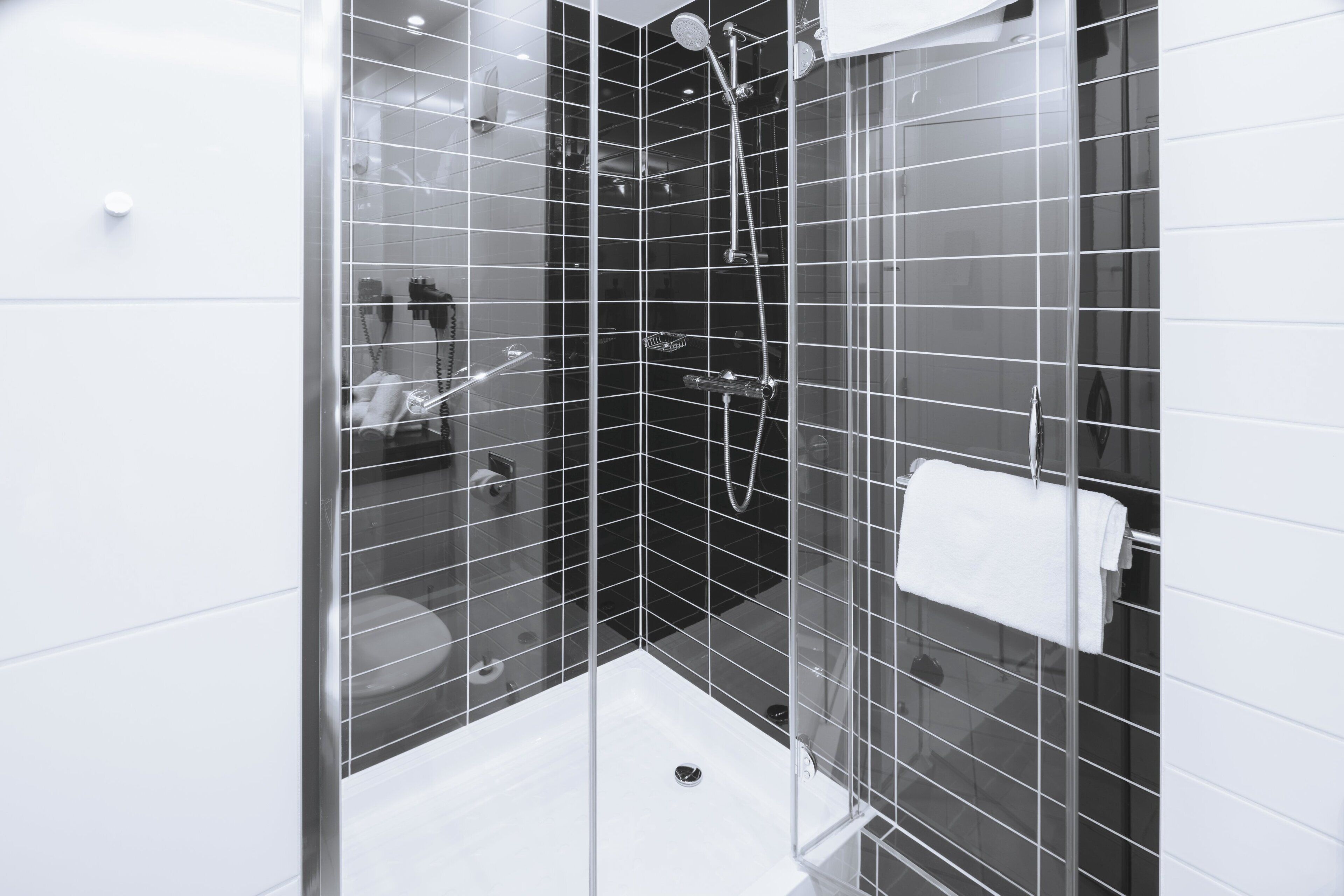 A modern bathroom with a glass shower enclosure, white tiles, and a visible towel rack.