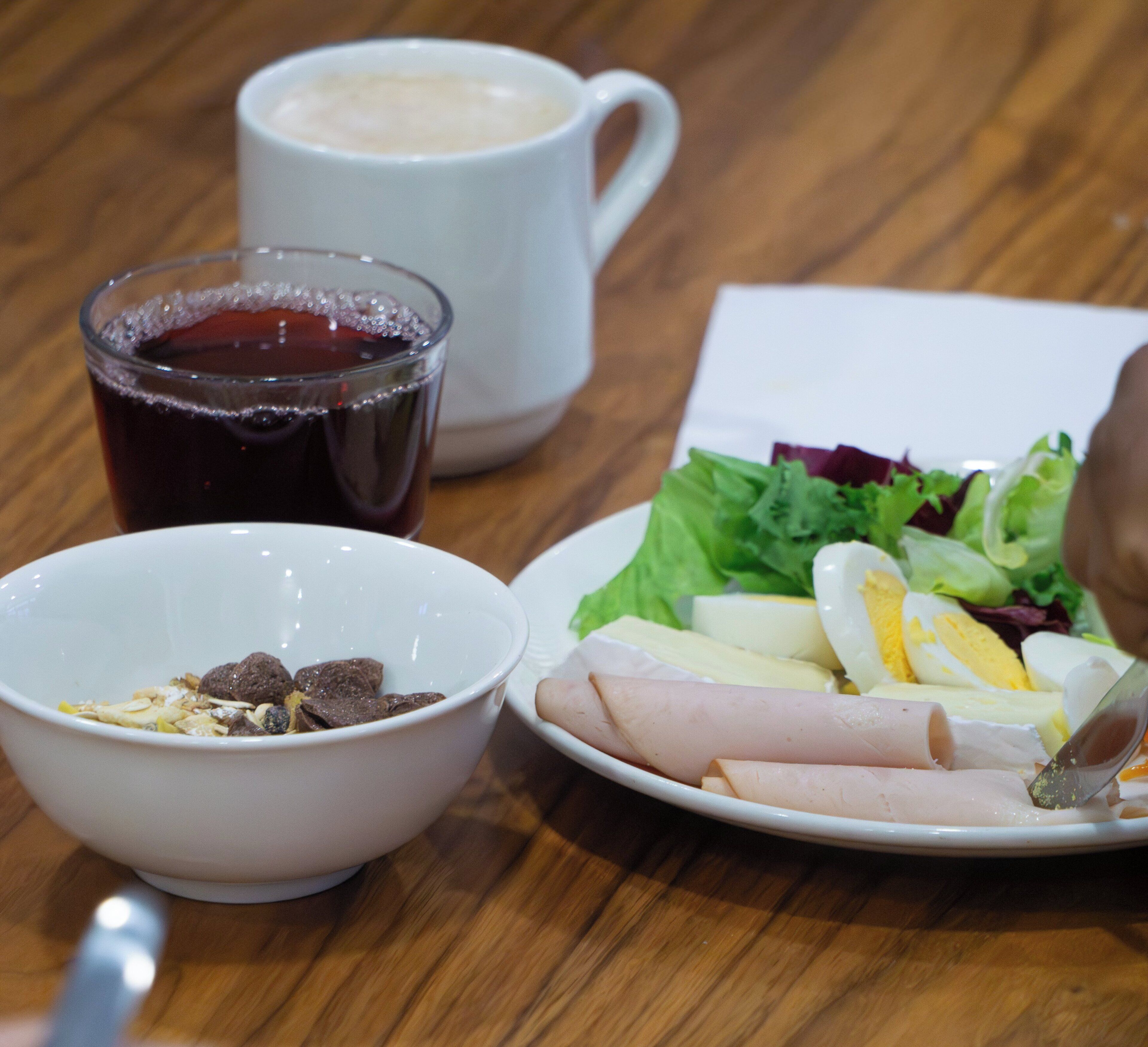 A table with a plate of food, a bowl of cereal, and a cup of coffee.