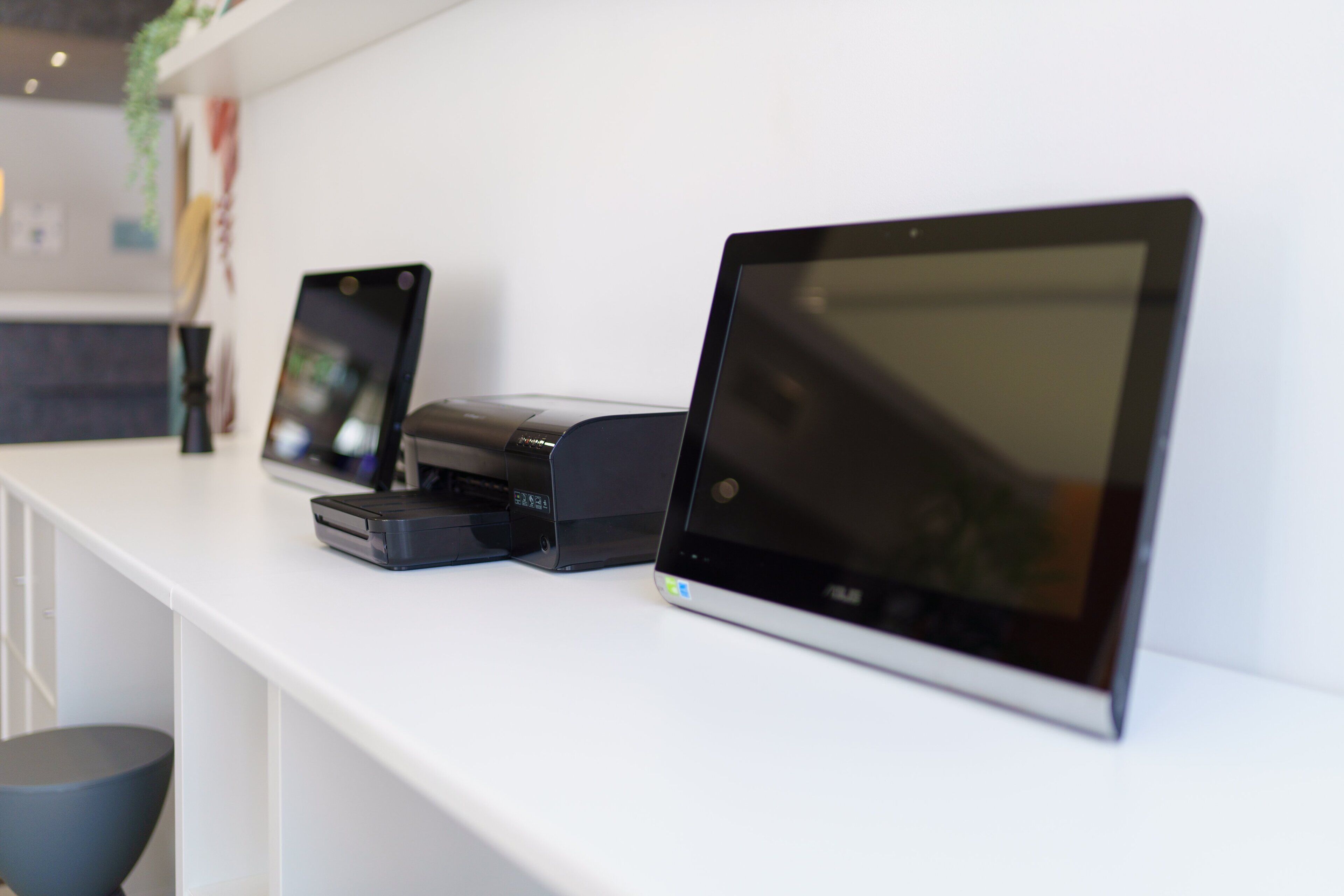 Ein weißer Tresen mit drei Geräten: einem Tablet, einem Drucker und einem Scanner.