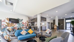 A modern hotel lobby with a blue sofa, grey armchairs, a flat-screen TV, a bar area, and a large window. - Holiday Inn Express Strasbourg - Centre by IHG (Strasbourg)