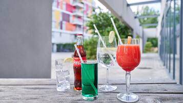 A wooden table with four drinks: a Coca-Cola bottle, a green drink, a red drink with a lemon slice, and a clear drink with a straw.