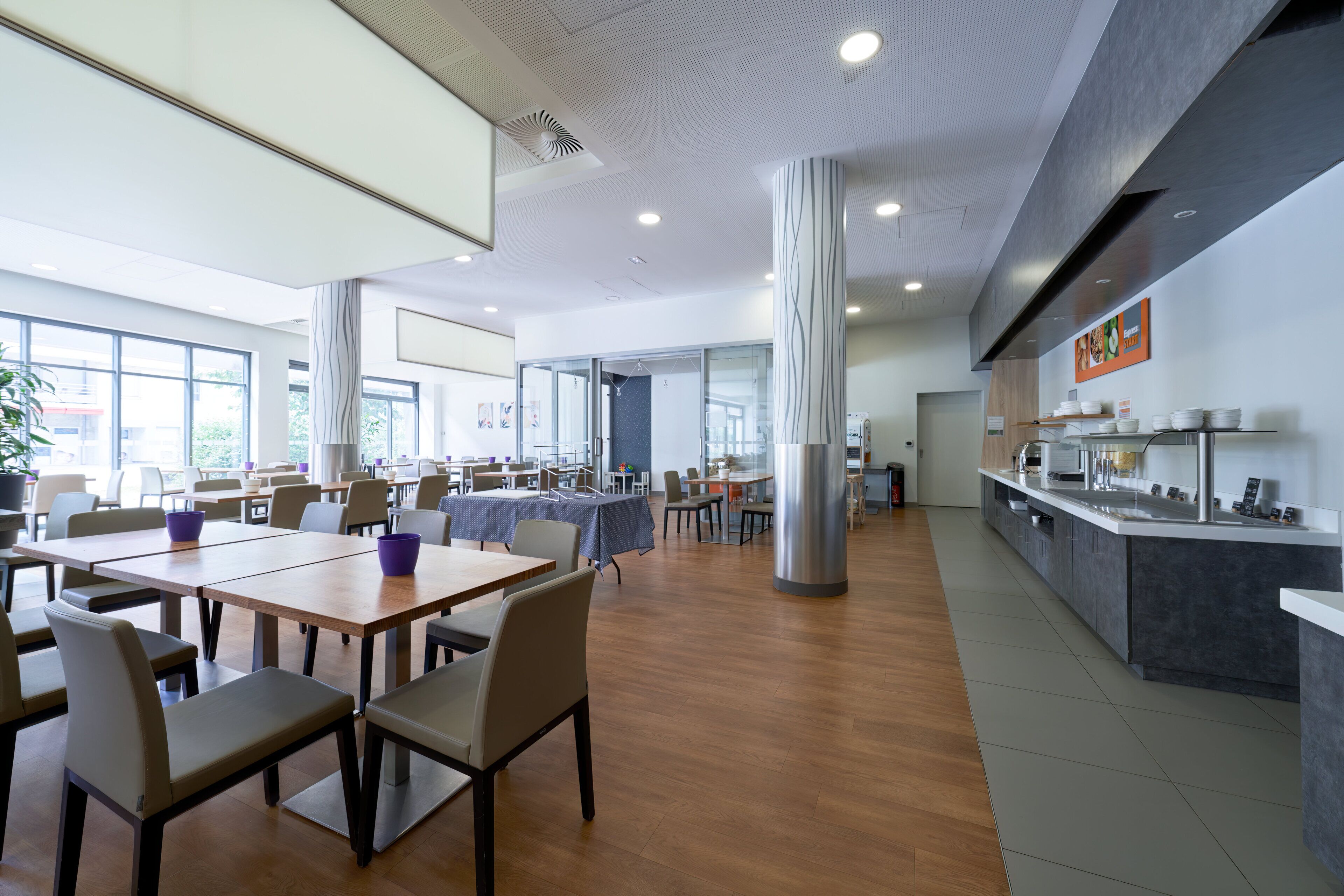 A spacious dining area with tables and chairs, a kitchen counter, and large windows providing natural light.